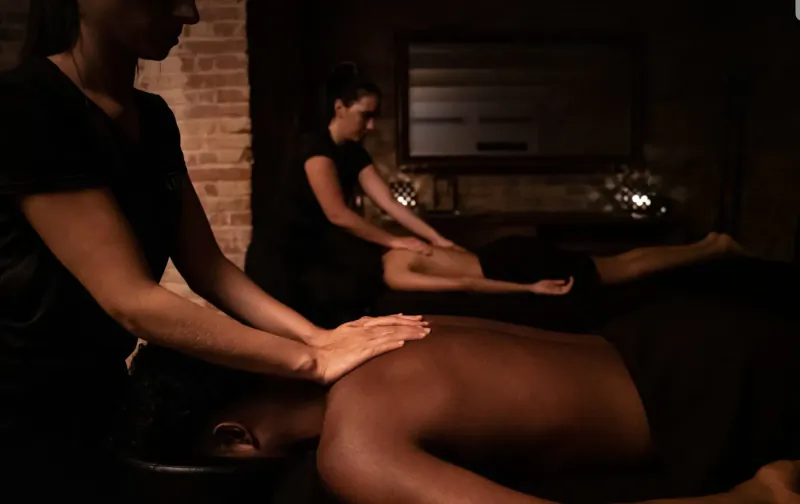 Two masseuses giving a neck and shoulder massage to a man lying face down at Aire Ancient Baths spa.
