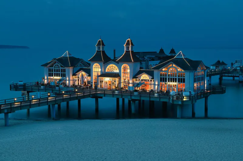 Lit white resort pier building with towers on beach at dusk, ideal wedding venue