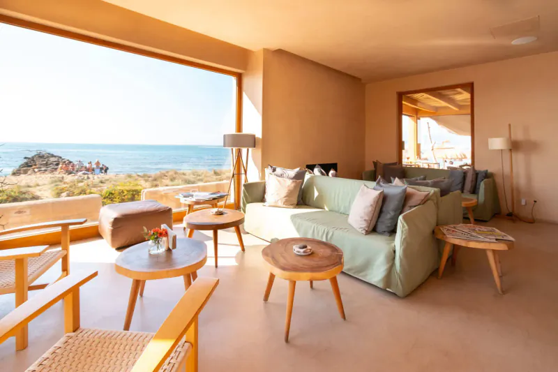 Cozy Gastro Beach lounge in Palma with green sofas, wooden tables, lamps, and sea view through large windows.