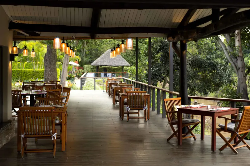 Spacious wooden veranda at The Norfolk Nairobi with tables, chairs, lanterns, and lush jungle view.