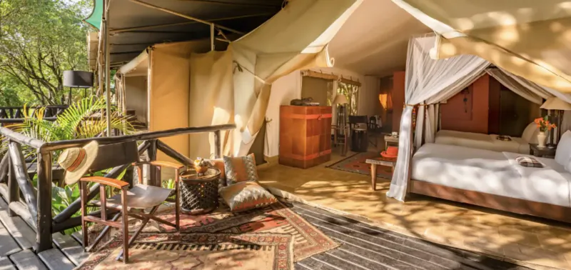 Luxurious Fairmont Mara Safari Club tent with canopy bed, wooden furniture, and deck overlooking lush greenery.