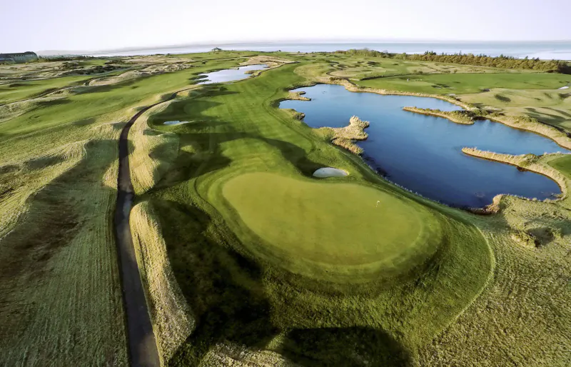 Aerial view of Fairmont St Andrews golf course in Scotland with lush greens, bunkers, ponds, and ocean horizon.