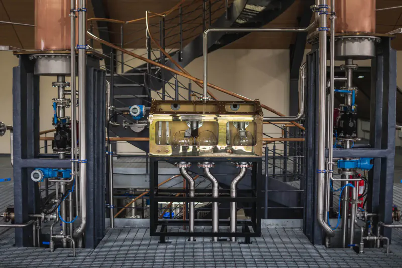 Industrial whisky distillery with copper stills, pipes, and metal staircase in production hall