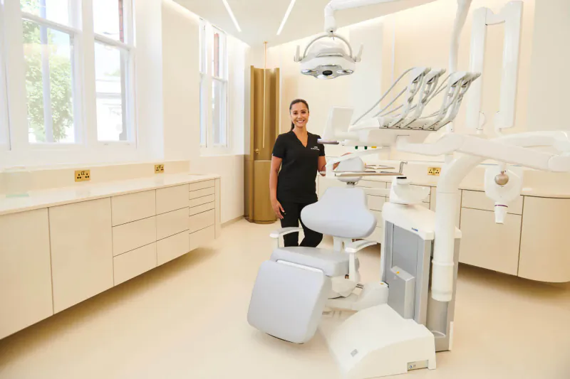 Dr Manrina Rhode, top UK cosmetic dentist, standing by modern dental chair in clinic