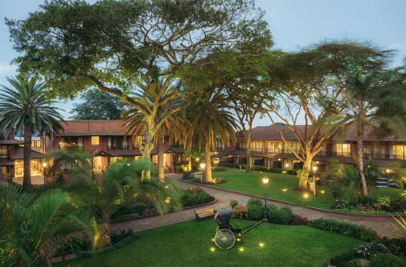 Fairmont The Norfolk, Nairobi: Elegant terracotta buildings with palm trees, lush gardens, and lanterns at dusk.