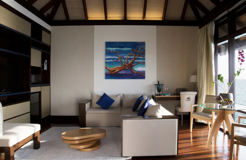 Luxurious Coco Bodu Hithi villa interior with ocean view, blue octopus wall art, beige sofa, and wooden furniture.