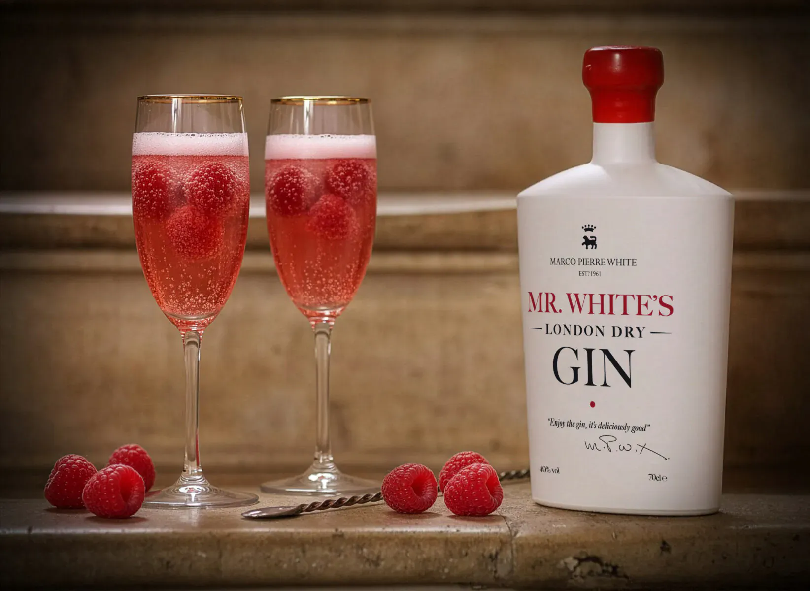 Two glasses of pink raspberry fizz with Mr. White’s M.R. White’s London Dry Gin bottle, garnished with fresh raspberries.