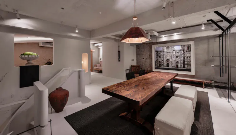 Stylish contemporary restaurant interior with rustic wooden dining table, white stools, pendant light, and large architectural wall art.