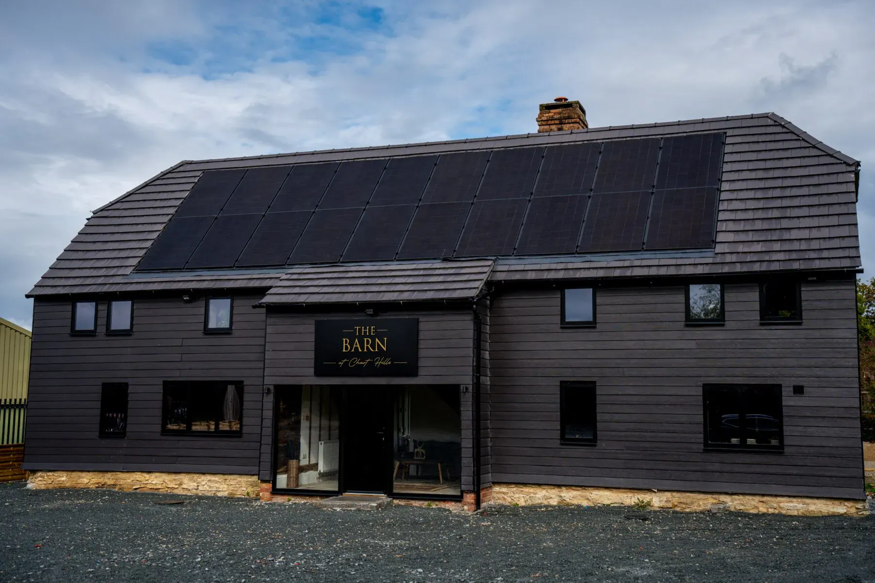 The Barn luxury accommodation at Chart Hills, dark barn-style building with solar panels on roof and entrance sign.