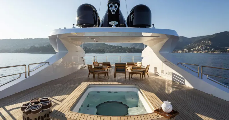Aft deck of luxury yacht ALFA with hot tub, lounge chairs, and coastal views at sunset.