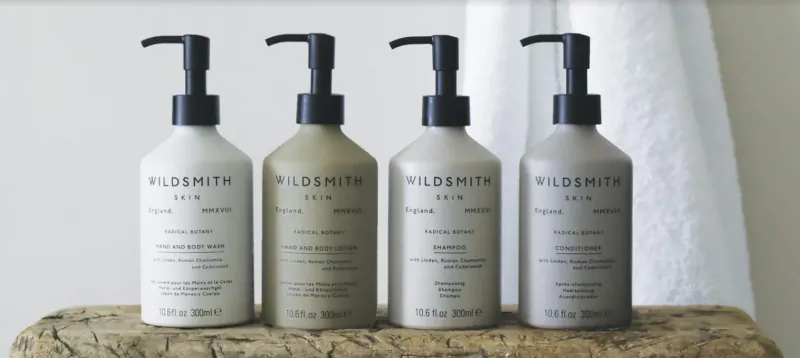 Four Wildsmith Skin pump bottles on wooden surface: Treehouse, Body Wash, Body Lotion, Body Cream.