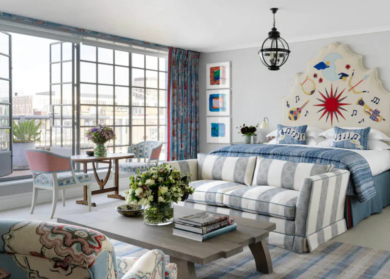 Chic Soho Hotel room with blue bed, striped sofa, flowers, art, large windows to balcony.