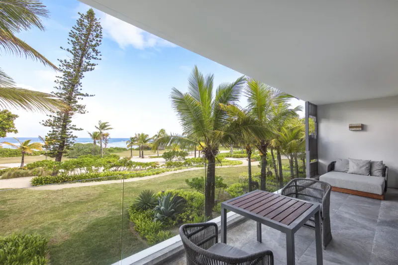 Spacious resort balcony with wooden table and chairs overlooking tropical gardens, palm trees, and ocean at Anantara Iko Mauritius.