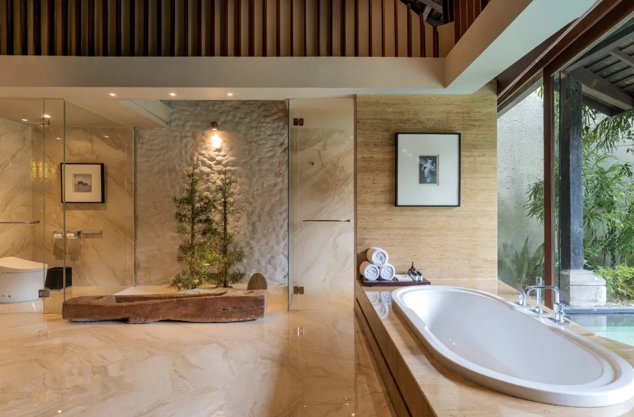 Exquisite modern bathroom at Ametis Villas Canggu Bali with freestanding tub, glass shower, wood bench, towels, plants, and lush views.