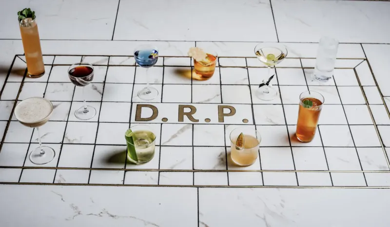 Assortment of cocktails in glasses on checkered marble surface with 'D.R.P.' text, Disrepute Bar oxymorons menu