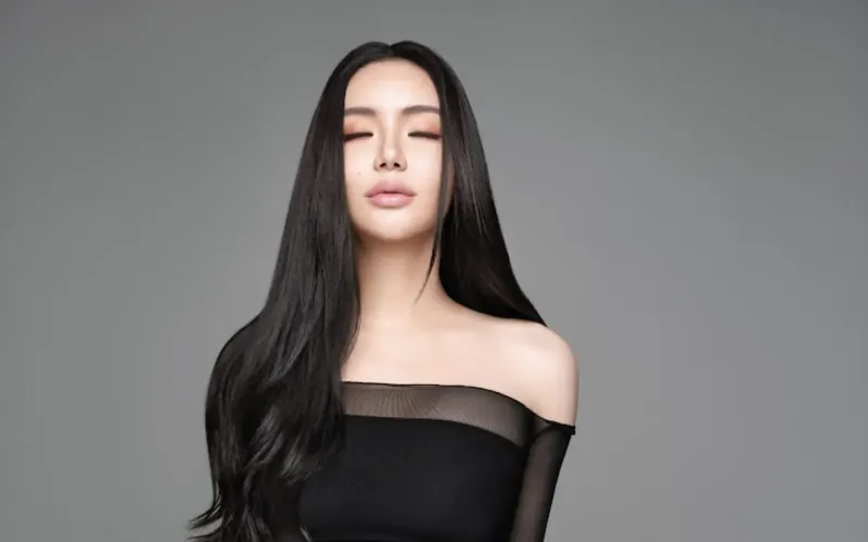 Kim Lim with long black hair, serene expression, off-shoulder black top, gray background