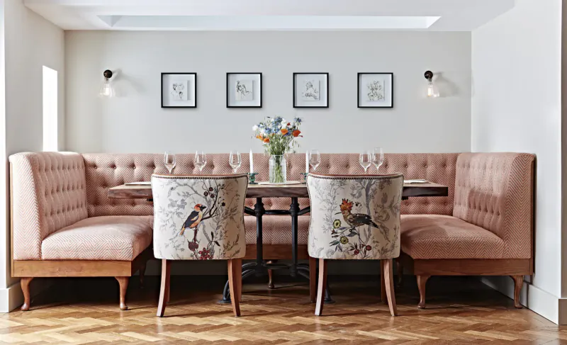 Elegant pink upholstered booth seating with bird-patterned chairs and floral centerpiece in luxury lounge with art and wall lamps