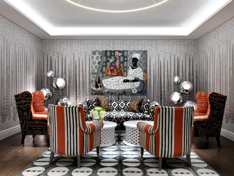 Chic Soho Hotel room with abstract African figure artwork, orange striped armchairs, white tables, and modern lighting on silver walls.
