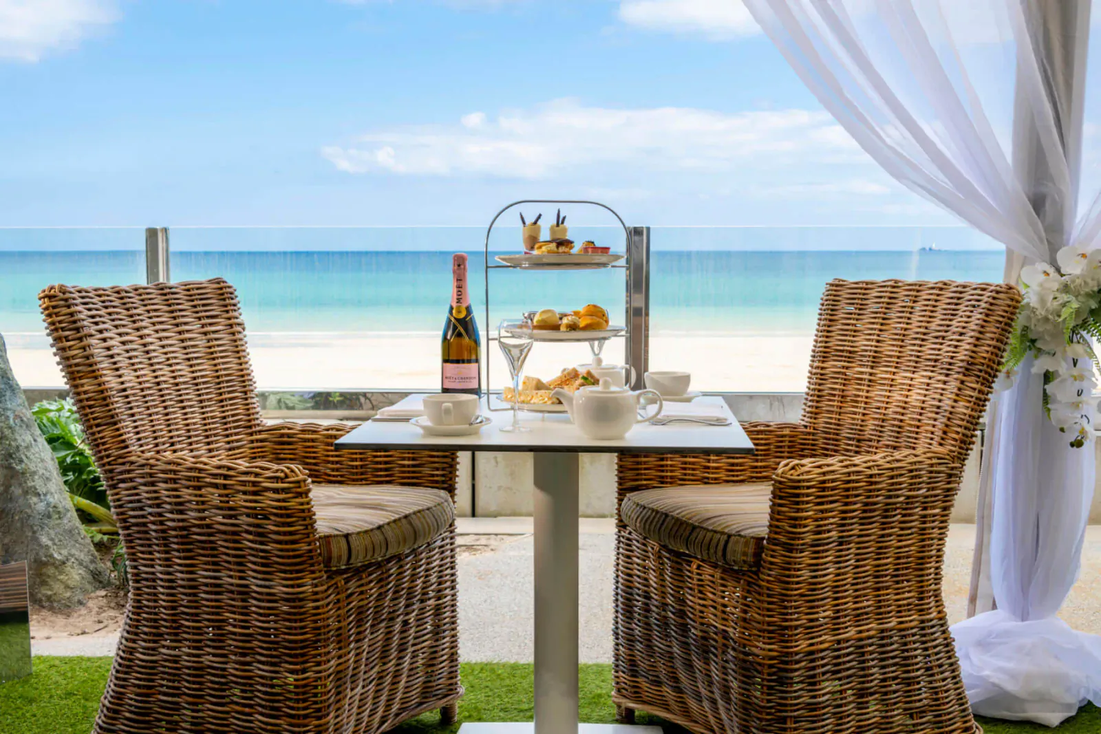 Outdoor table with Moët & Chandon champagne, tiered scones, tea overlooking beach under sheer drapes.
