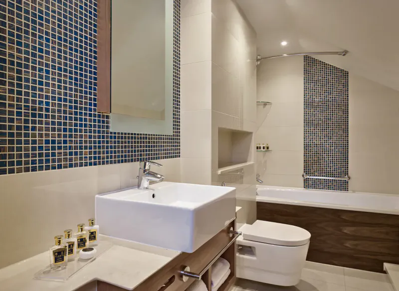 Luxury hotel bathroom with blue mosaic tiles, white sink, bathtub, shower, and toilet at 100 Queen’s Gate Hotel