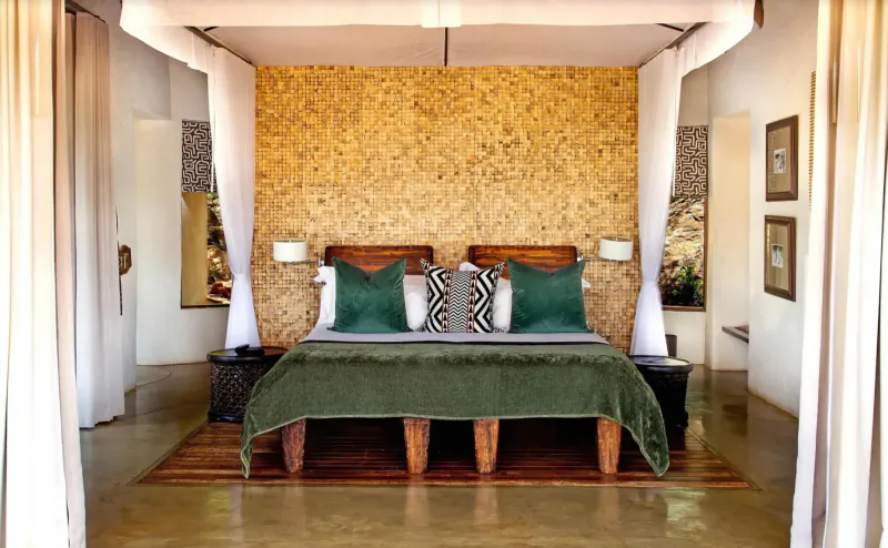 Luxurious king bed with green duvet and pillows under beige textured canopy in Madikwe Hills lodge room