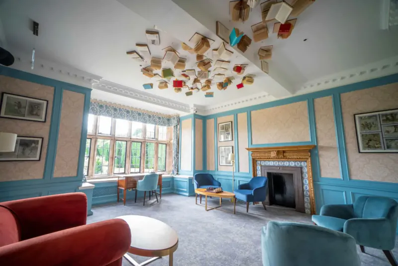 Elegant Billesley Manor Hotel lounge with blue walls, red armchairs, fireplace, and colorful book art hanging from ceiling.
