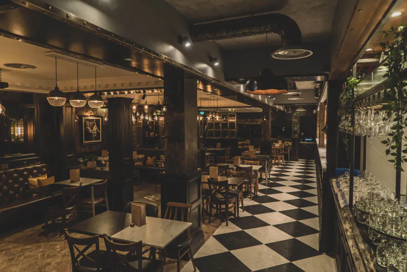 Six by Nico restaurant interior with black-and-white checkered floor, wooden tables, pendant lights, and plants.