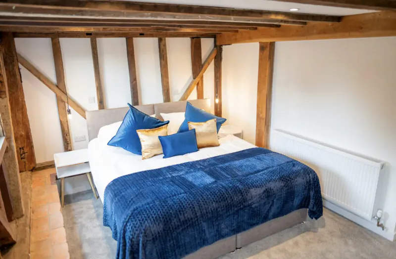 Luxurious king bed with blue pillows and duvet in timber-framed barn bedroom at Chart Hills The Barn