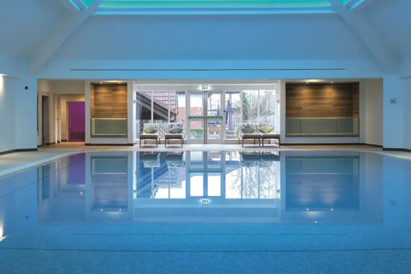 Spacious indoor swimming pool at Bristol Aztec Hotel and Spa with lounge chairs, glass doors to garden, and teal skylight.