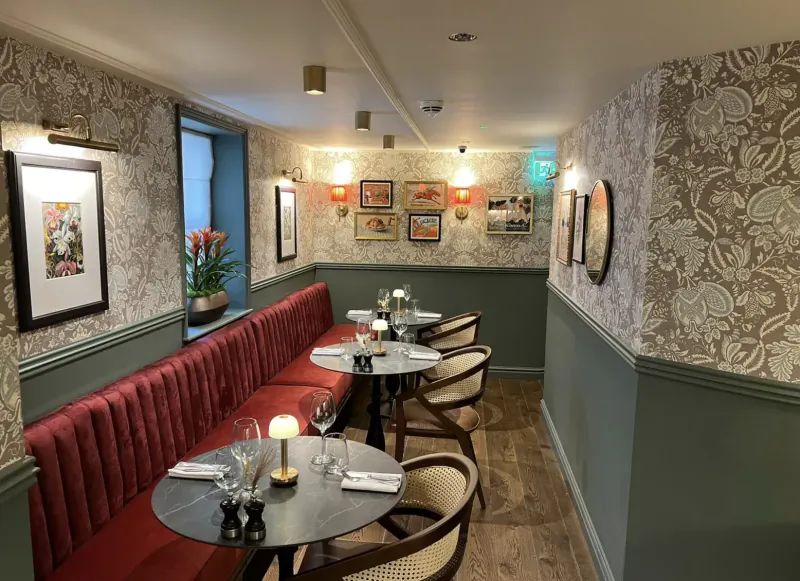 Elegant Brasserie Beau Bath interior: red velvet booth, round tables set with candles and wine glasses, ornate wallpaper, art.