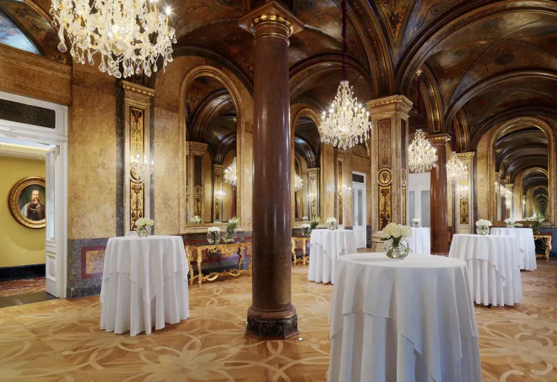 Opulent Gallery at Hotel Imperial Vienna with chandeliers, vaulted ceilings, columns, mirrors, and white-clothed round tables.