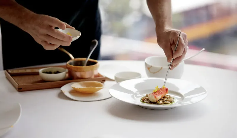 Chef at Saint Pierre sprinkles seasoning from small bowl onto plated pink crab dish on elegant table.