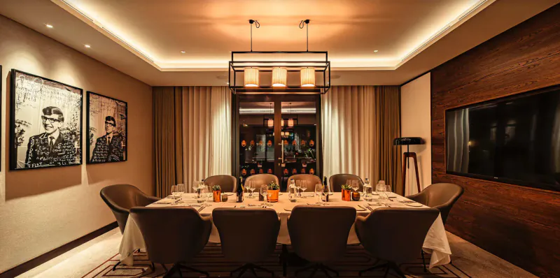 Elegant dining room in luxury apartment with large table set for dinner, wine bottles, warm lighting, and portraits on wood-paneled walls.
