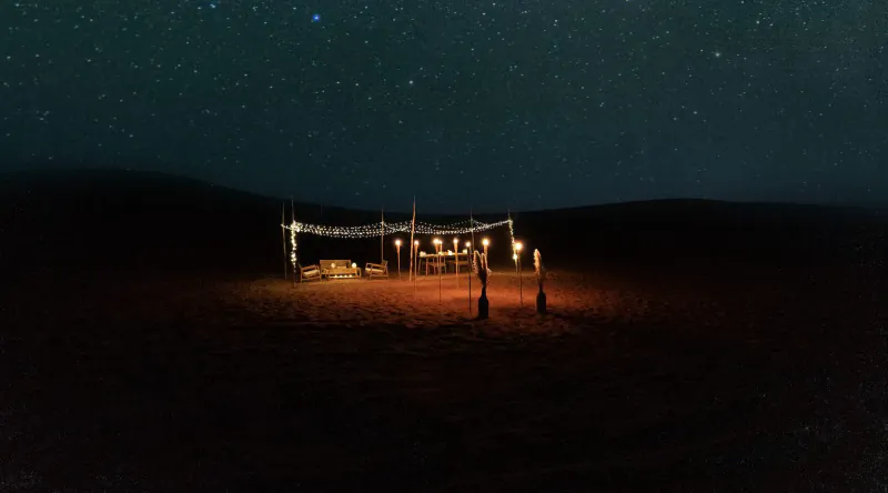 Lit tent with string lights in starry desert dunes at night, luxury Zerzura camp.