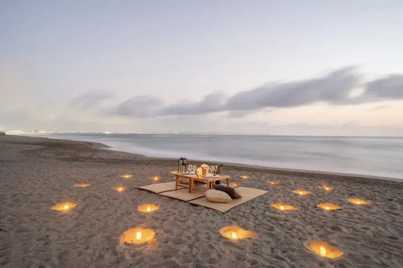 Romantic candlelit beach picnic table at dusk with lanterns on sand, Ametis Villa Bali