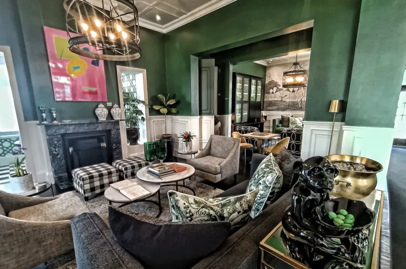Elegant green lounge with fireplace, plush seating, abstract pink art, plants, and brass Buddha statue