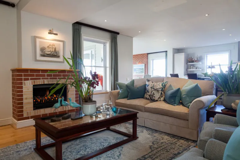 Cozy living room at Tintswalo Boulders with brick fireplace, beige sofa with teal pillows, plants, and wooden coffee table