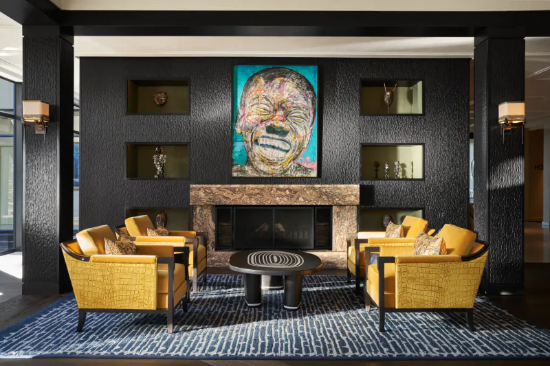 Luxury lounge at Delaire Graff Estate with vibrant portrait, yellow armchairs, stone fireplace, and modern decor.