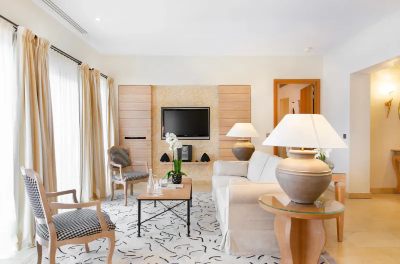 Elegant 5-star hotel living room with white sofa, armchairs, TV, lamps, orchids, and Provence-style decor.