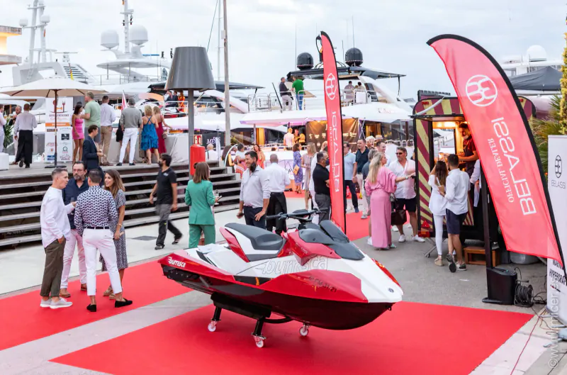 Red and white Sea-Doo Spark jetski on red carpet at crowded marina event with banners and people.