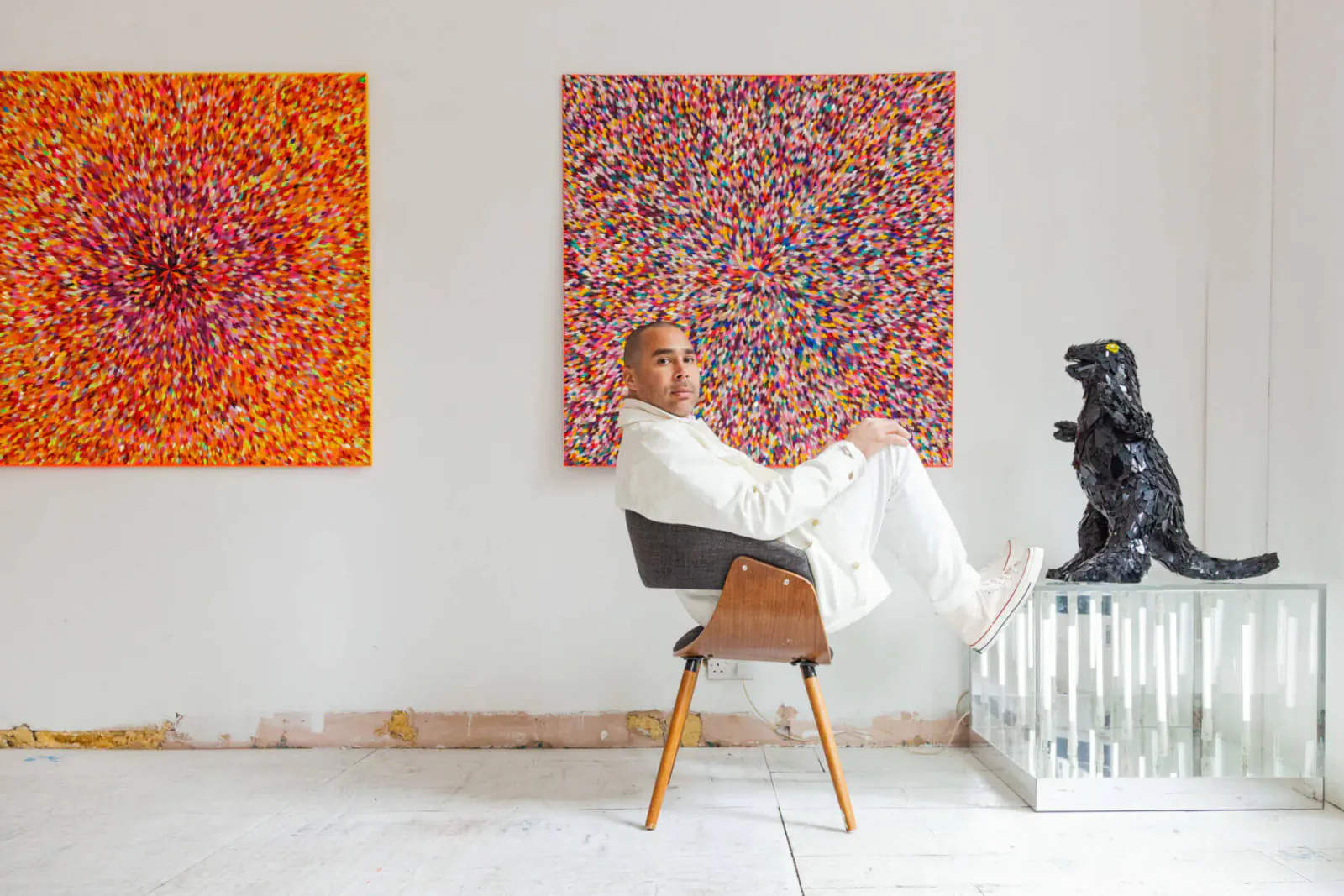 Robi Walters in white suit, lounging in chair beside black T-Rex sculpture in colorful abstract art gallery