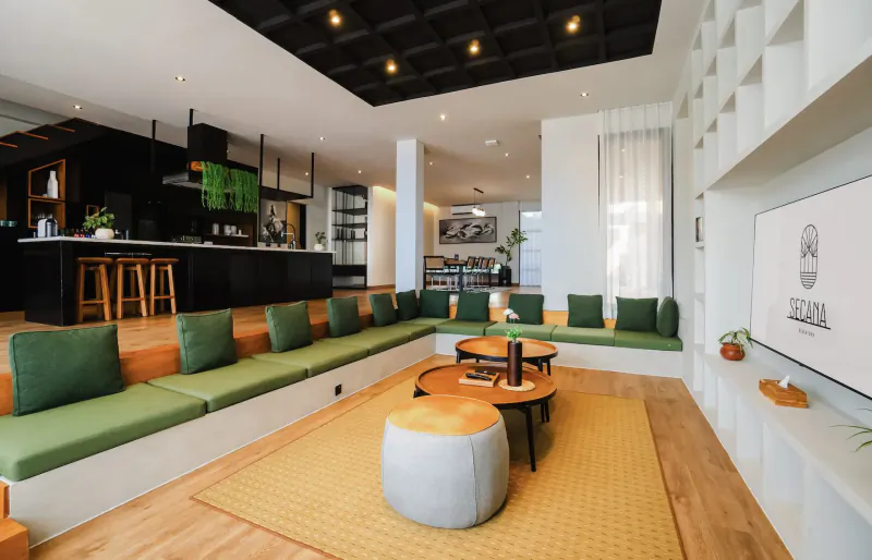 Modern lounge in Secana Beachtown Bali with green L-shaped sofa, wooden table, bar kitchen, and shelves