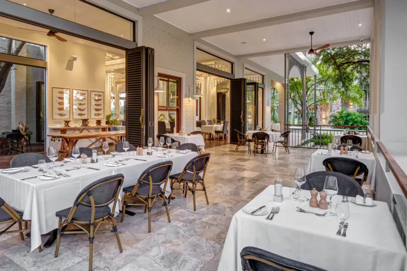 Elegant outdoor terrace at Palm River Hotel with white-clothed dining tables, rattan chairs, large windows, and garden views near Victoria Falls.