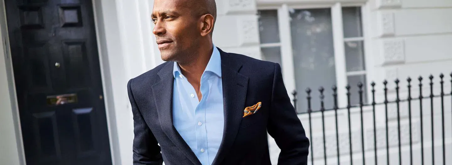 Man in navy suit with blue shirt and pocket square stands by black door outside white townhouse, Charles Tyrwhitt Spring Collection featured