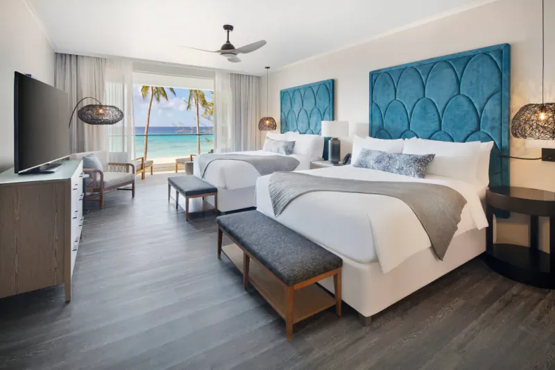 Luxury beachfront hotel room with two queen beds, turquoise headboards, balcony view of palm trees and ocean at O2 Beach Club & Spa.