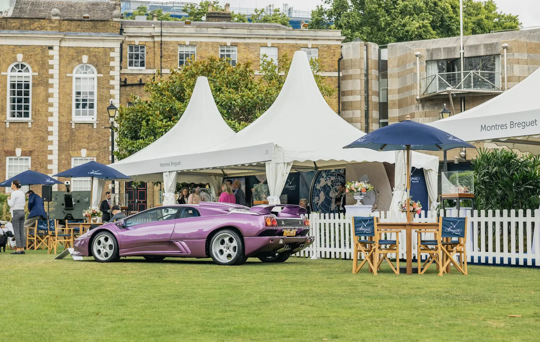 Purple Lamborghini parked on green lawn at London Concours 2024, with white tents, blue umbrellas, and people nearby