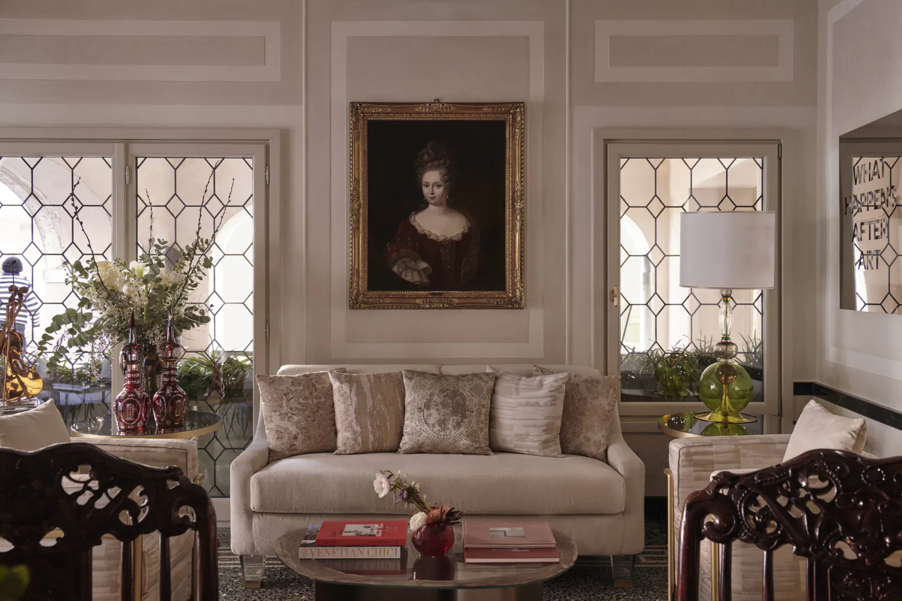 Elegant hotel lounge at Violino d’Oro Venice with cream sofa, ornate portrait, lamps, and floral arrangements by arched windows.