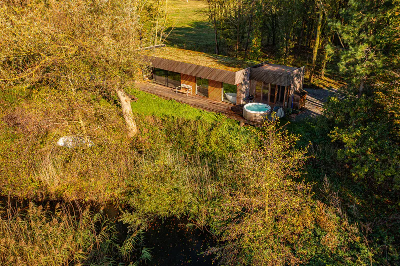 Aerial view of modern wooden glamping cabin with hot tub in autumnal Essex woodland setting.