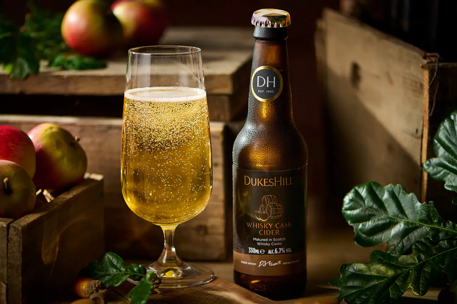 Dukeshill whisky cask cider bottle and sparkling glass beside apples in wooden crate