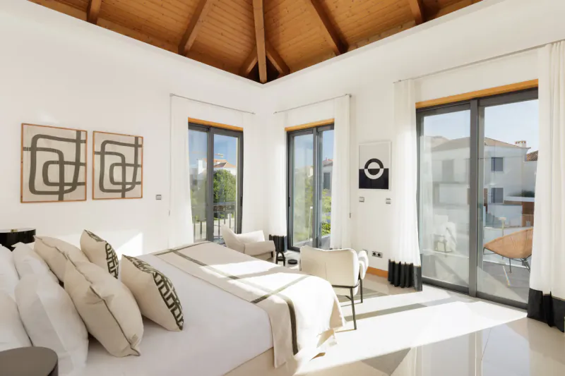 Spacious modern bedroom in Vale do Lobo resort with wooden ceiling, king bed, abstract art, and sliding doors to terrace.
